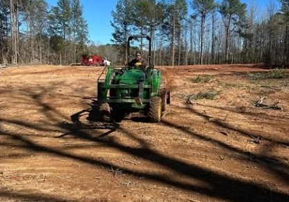Tractor working a cleared lot with pines in the background
